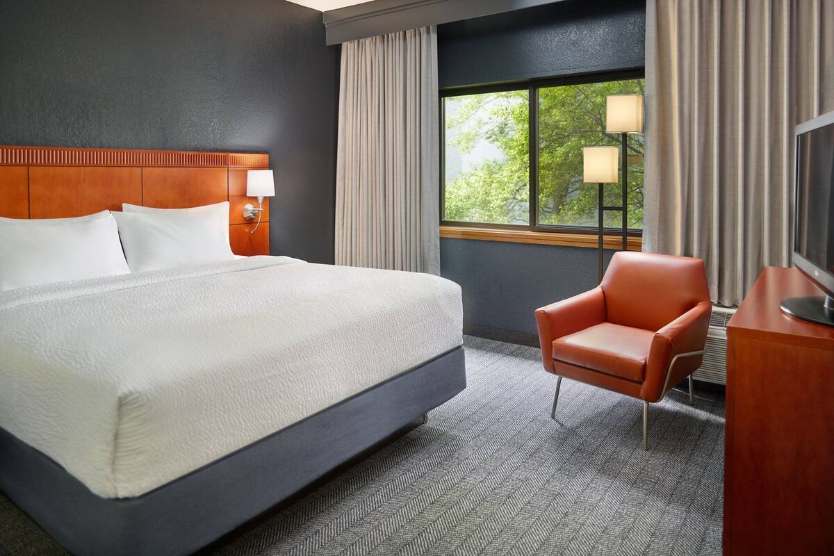 A hotel room with a large bed, a desk, a chair, a TV, and a window with curtains.