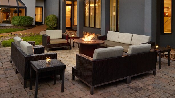An outdoor seating area with wicker furniture, a central fire feature, and a view of the building's interior. - Courtyard by Marriott Nashville Brentwood (Brentwood)