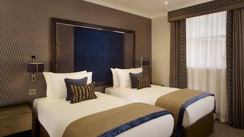 A hotel room with two beds, a large window with curtains, and a wall with a geometric pattern.