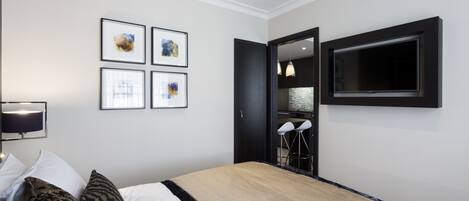 A modern hotel room with a large bed, a flat-screen TV mounted on the wall, and a small seating area with chairs.