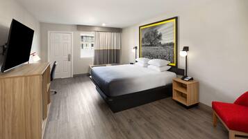 A hotel room with a bed, a desk, a TV, a chair, and a bedside table.