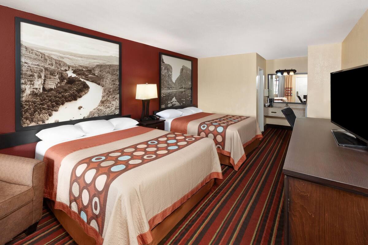 A hotel room with two beds, a TV, a desk, and a bathroom visible in the background.