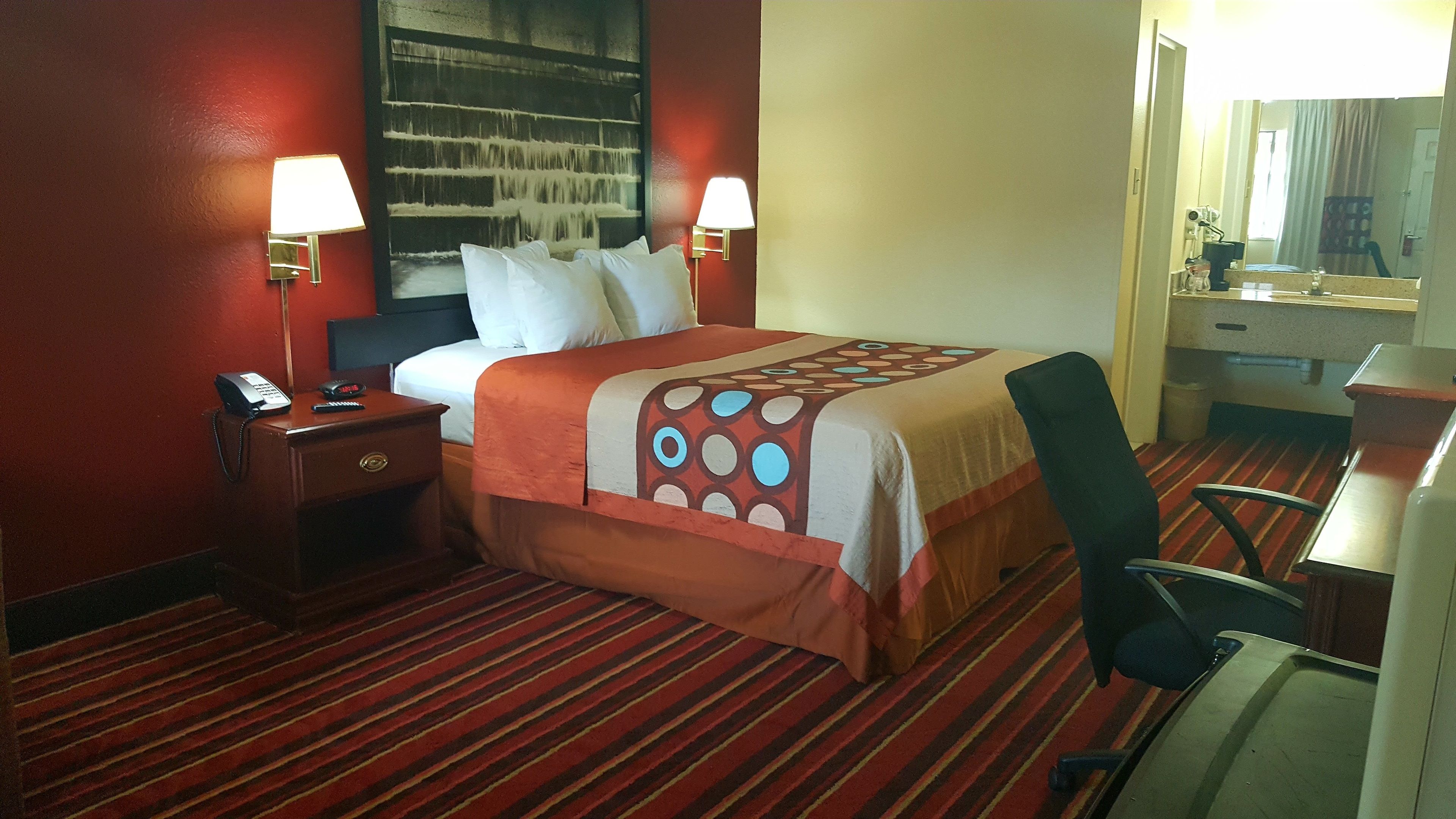 Una camera d'albergo con un letto, due lampade ai lati del letto, un telefono, una scrivania con una sedia e uno specchio.