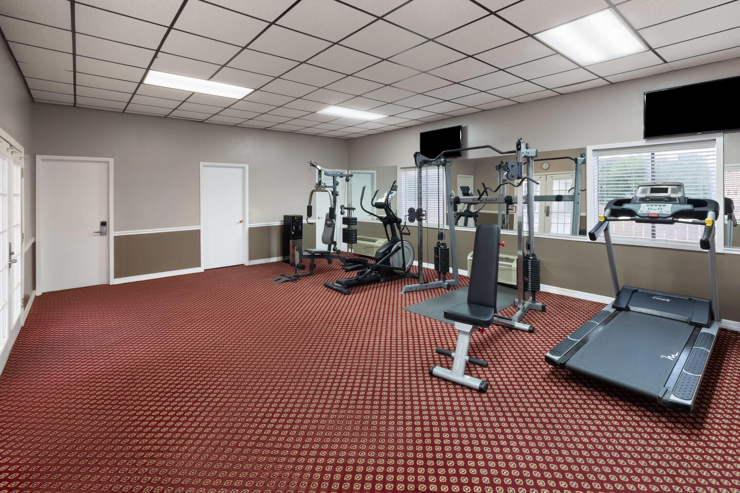 A gym with treadmills, weight machines, and a red patterned floor.