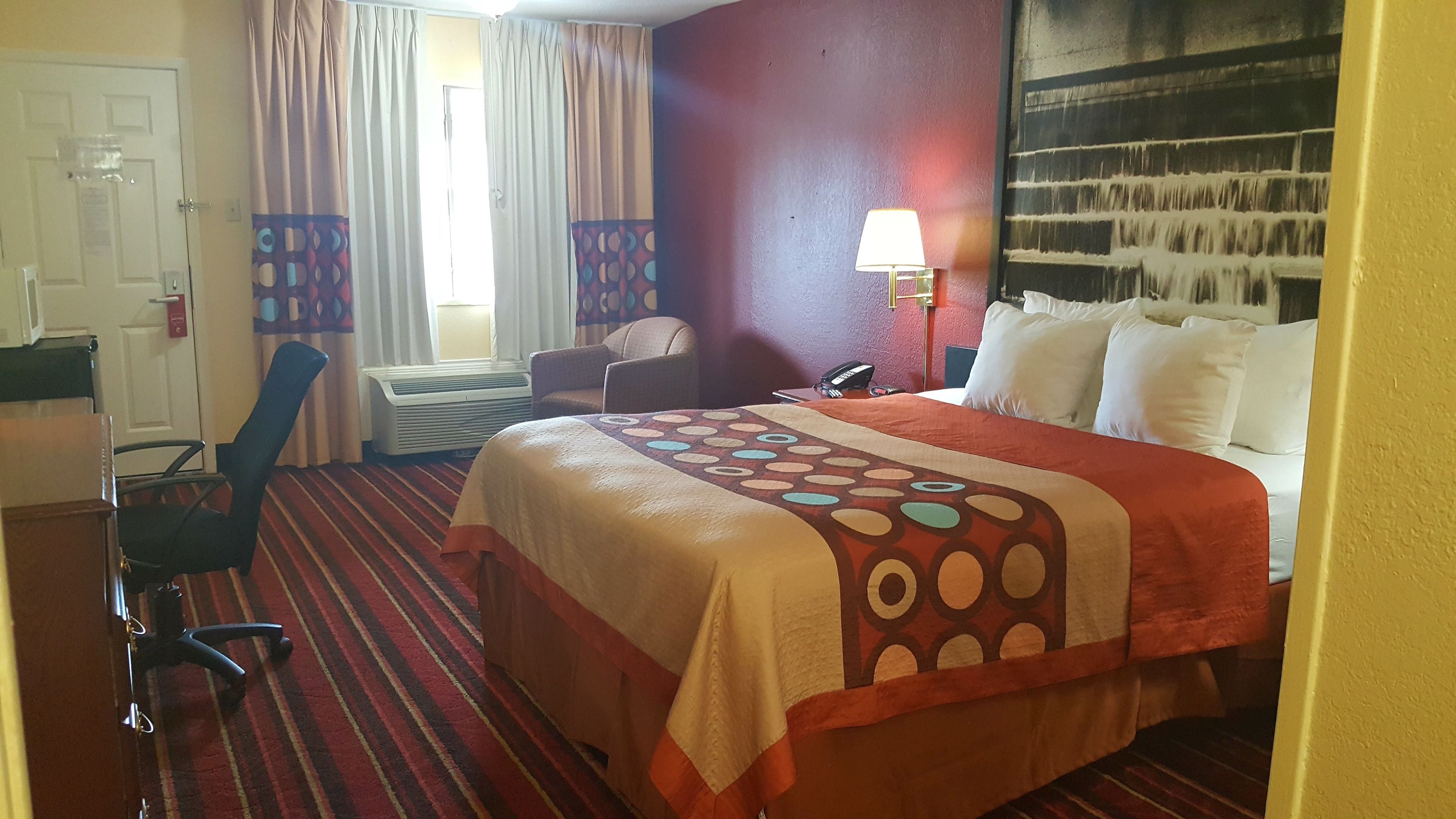 Una habitación de hotel con cama, una silla, un escritorio y un ventanal con cortinas.