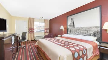 Habitación de hotel con una cama grande, un escritorio con televisor, una silla, una lámpara de escritorio y un cuadro grande en la pared.