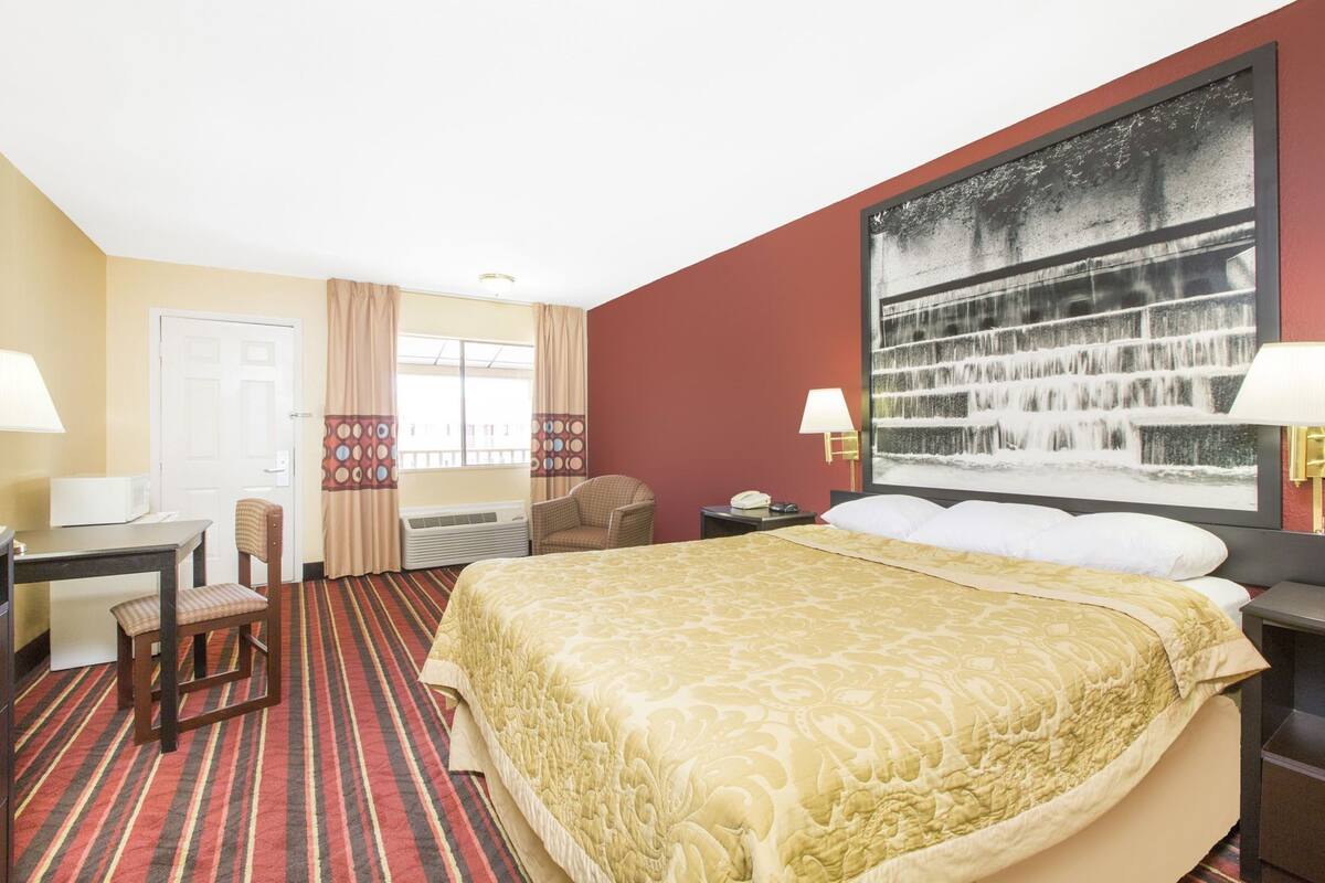 A hotel room with a bed, desk, chair, and a large window with curtains.
