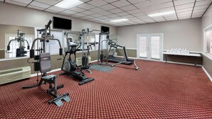 Un gimnasio con equipo de ejercicio, un televisor y suelo cubierto de alfombra roja.