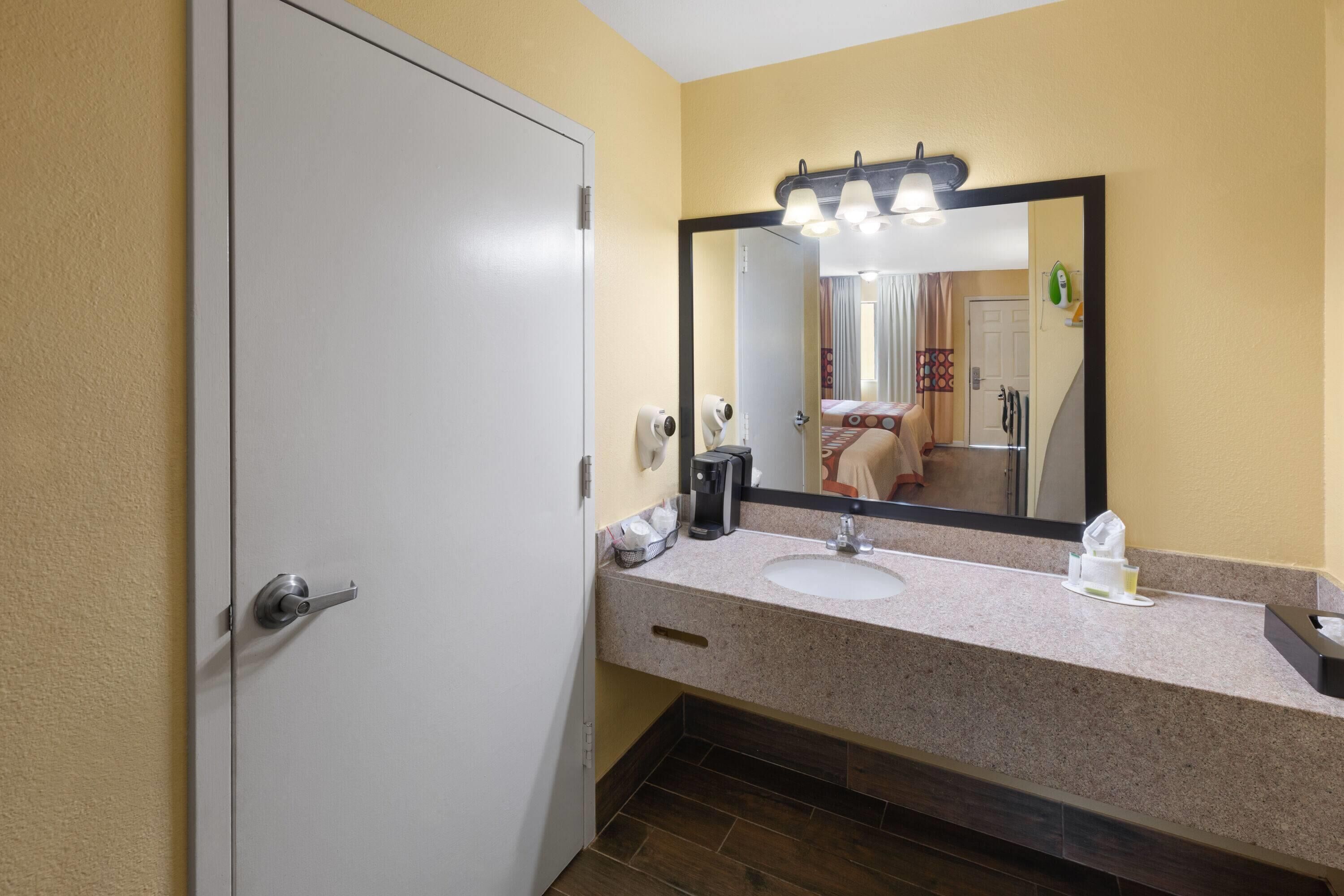A bathroom with a white door, a sink, a mirror, and a towel rack.