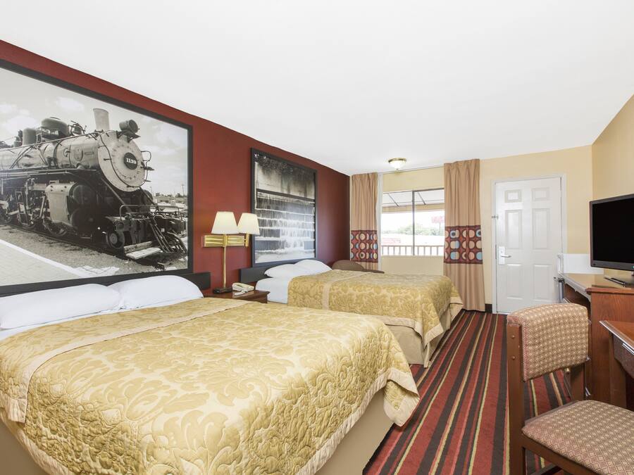 Habitación de hotel con dos camas, televisión, escritorio y un cuadro grande con una imagen de un tren.