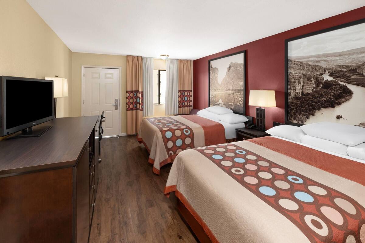 A hotel room with two beds, a TV, a desk, and a large window.