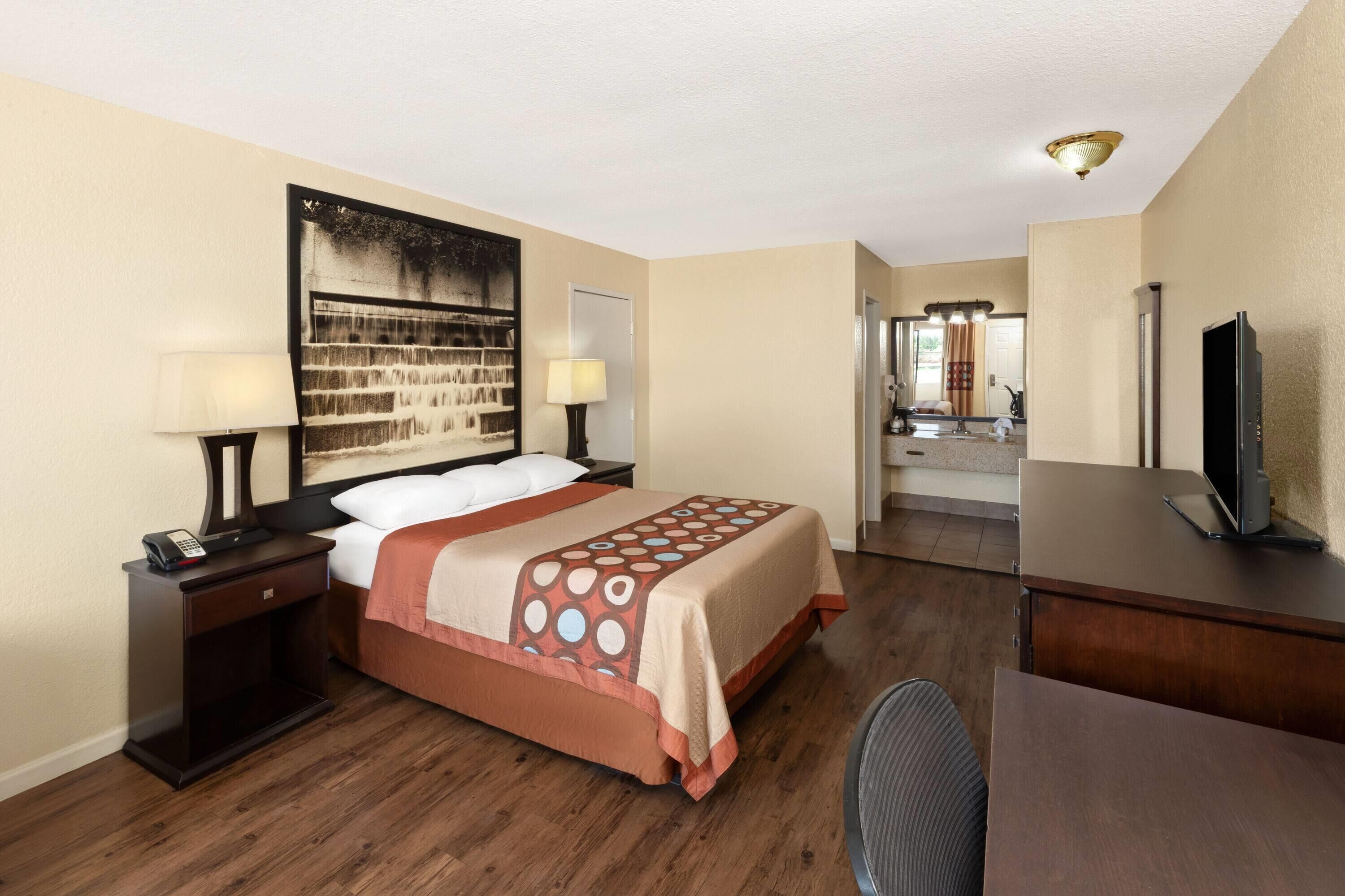 Una habitación de hotel con cama, mesitas de noche, escritorio, televisor y baño a la vista.