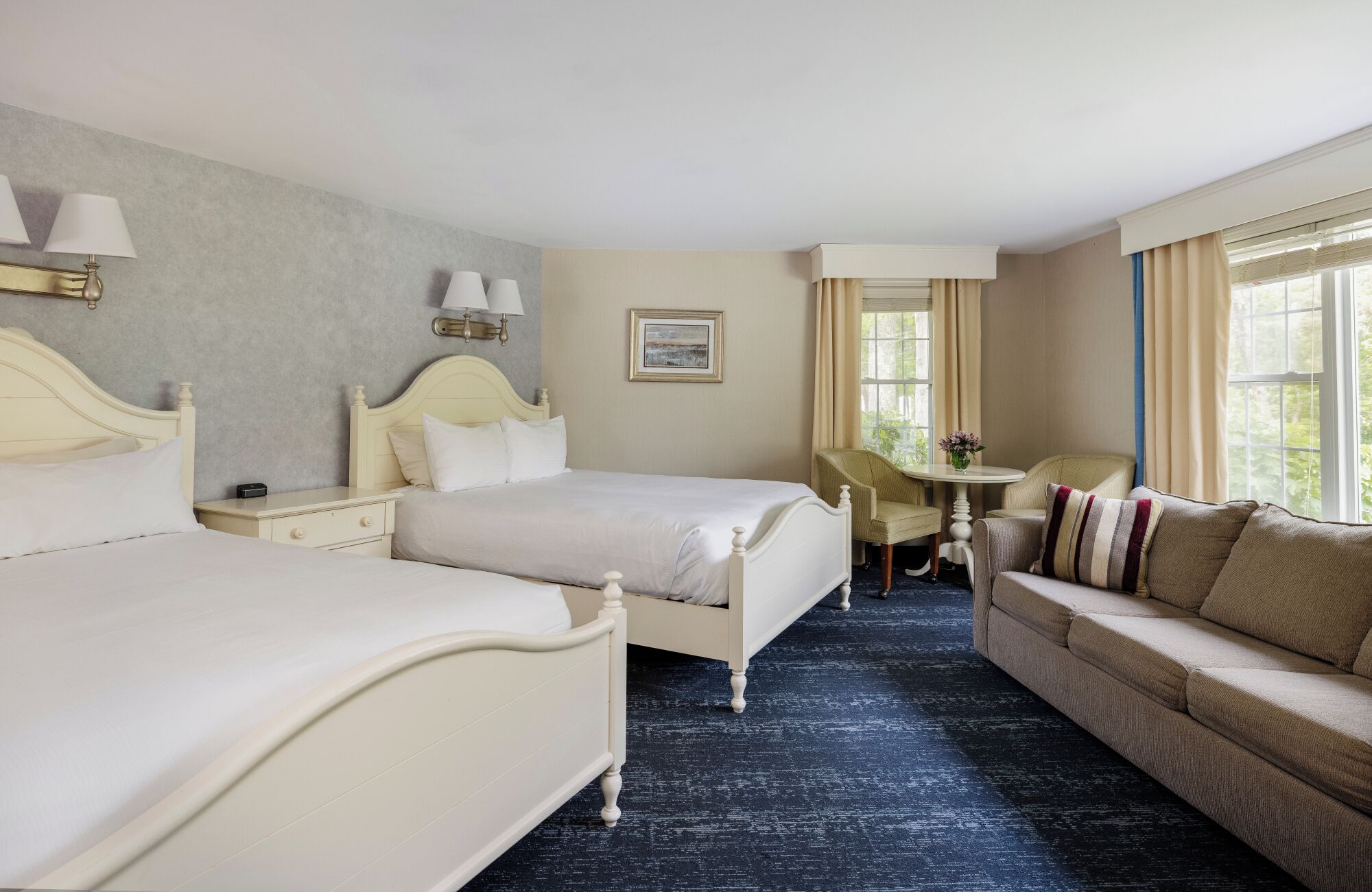A hotel room with two beds, a sofa, a small table, and a window with curtains.