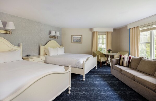 A hotel room with two beds, a sofa, a small table, and a window with curtains.