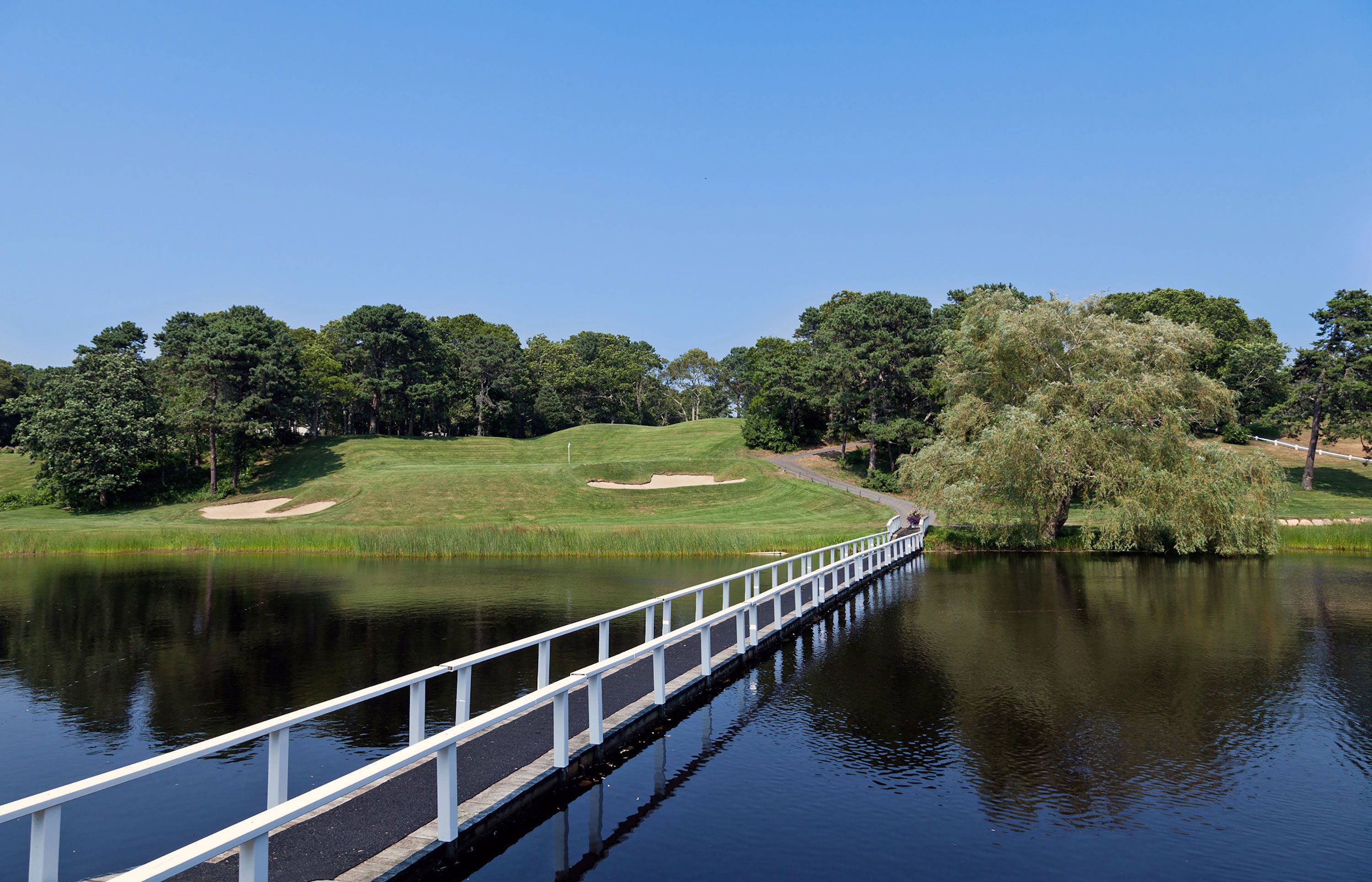 A bridge over a calm lake with a golf course in the background.