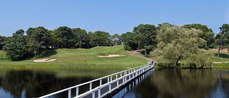A bridge over a calm lake with a golf course in the background.