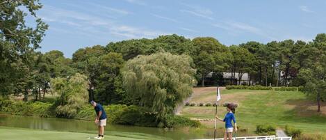 A golf course with a pond, trees, and a bridge.
