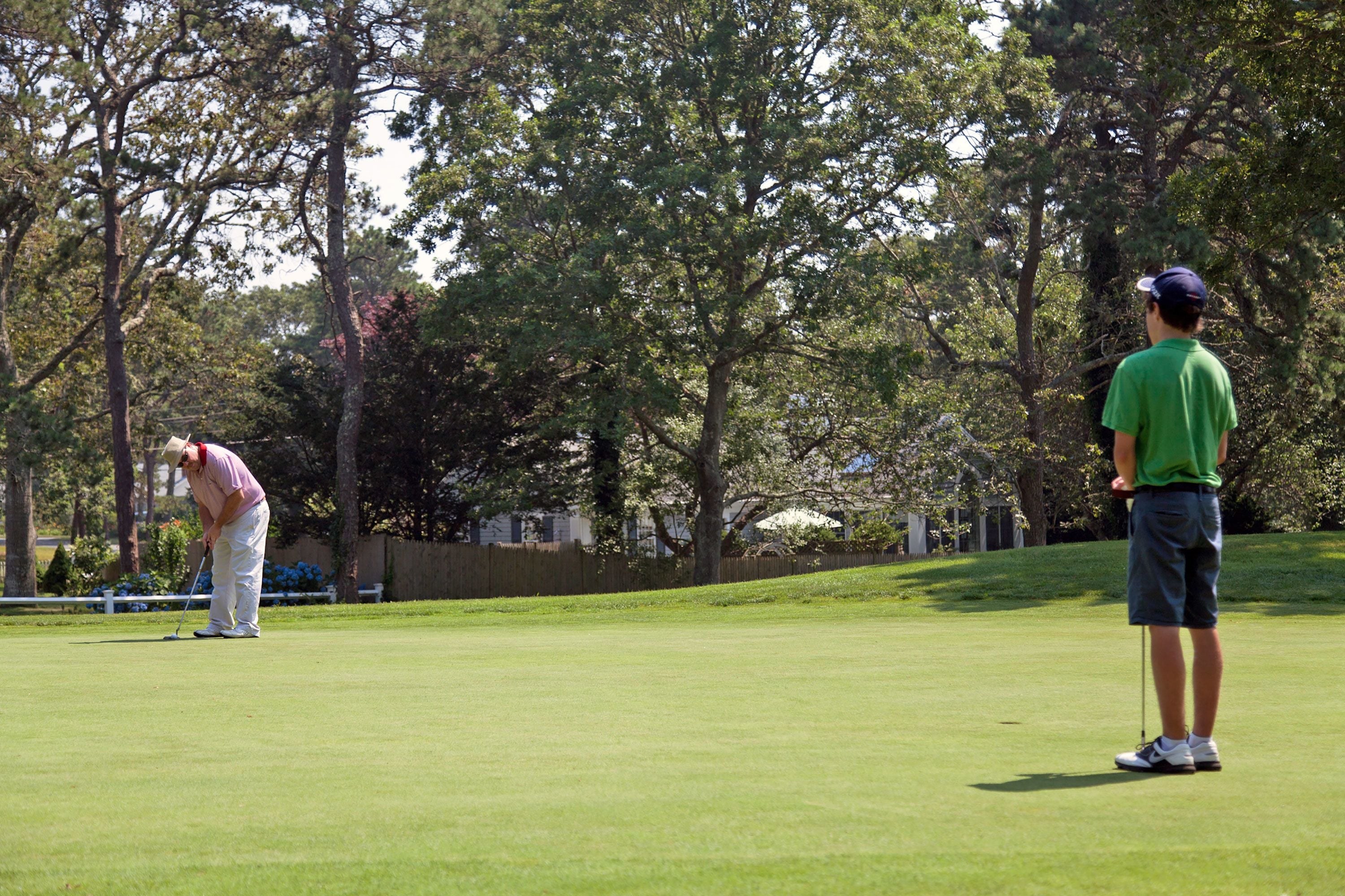 A golf course with a putting green, trees, and a fence in the background.