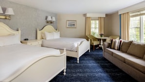 A hotel room with two beds, a sofa, a desk, and a window with curtains.