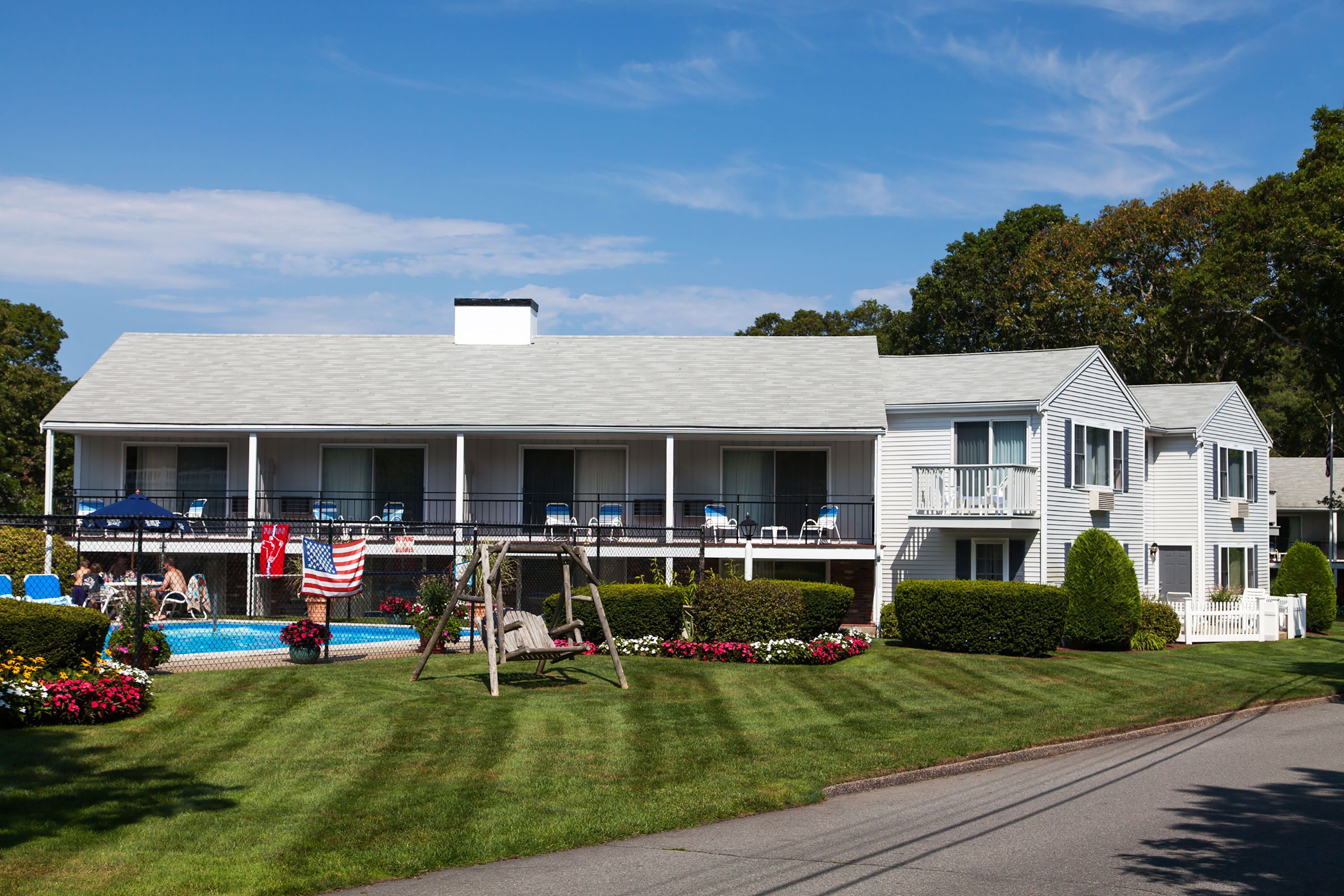 A two-story motel with a swimming pool, outdoor seating, and a flag.