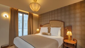 Une chambre d’hôtel avec un grand lit, deux tables de chevet avec des lampes, une fenêtre avec des rideaux et un luminaire fixé au mur.