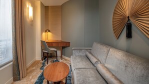 Une chambre d’hôtel moderne avec un canapé gris, un bureau en bois, une chaise et une table basse ronde.