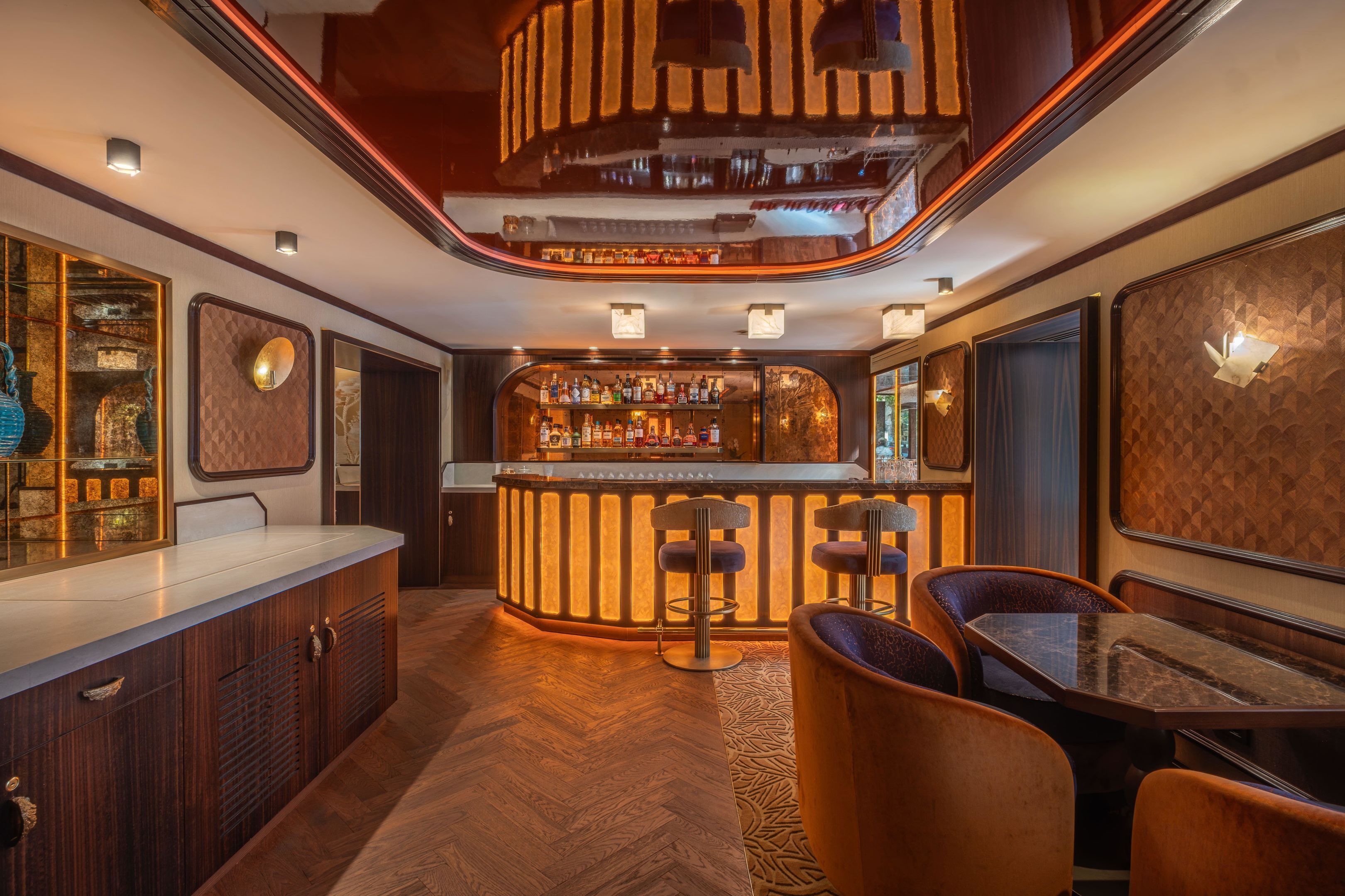 A bar area with a wooden counter, bar stools, and a variety of bottles.