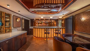 A bar area with a wooden counter, bar stools, and a variety of bottles.