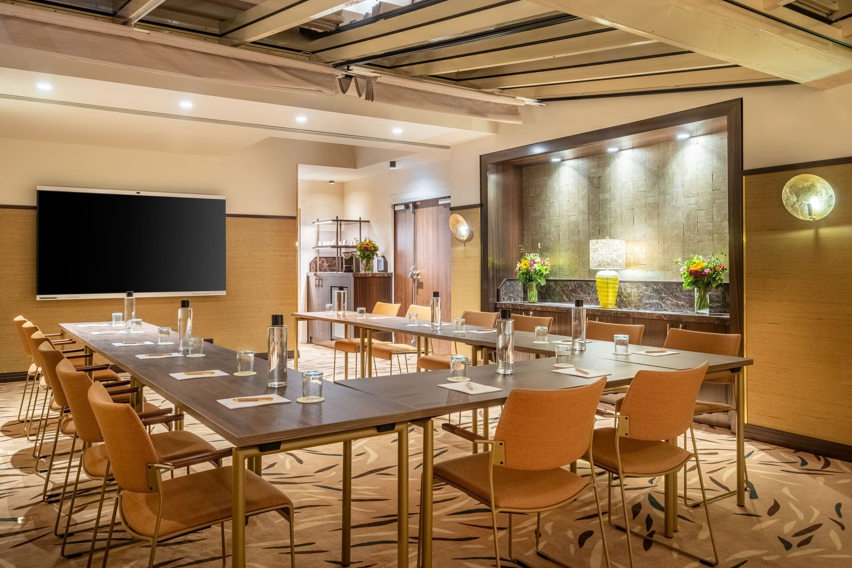 A conference room with a long table, chairs, a projector screen, and a large mirror.