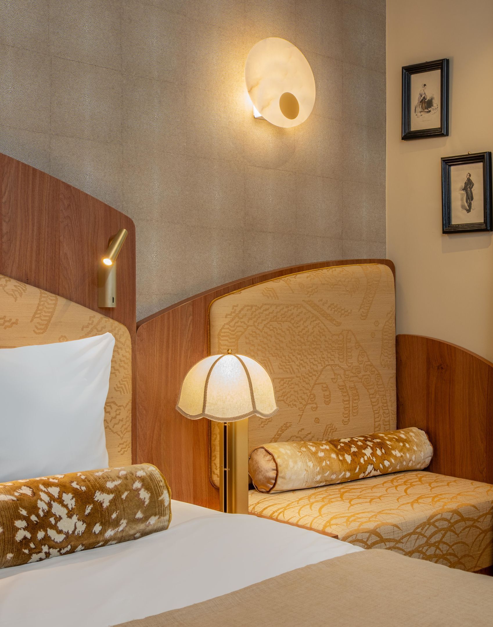 Quarto de hotel com cabeceira de madeira, luminária de cabeceira e duas molduras na parede.