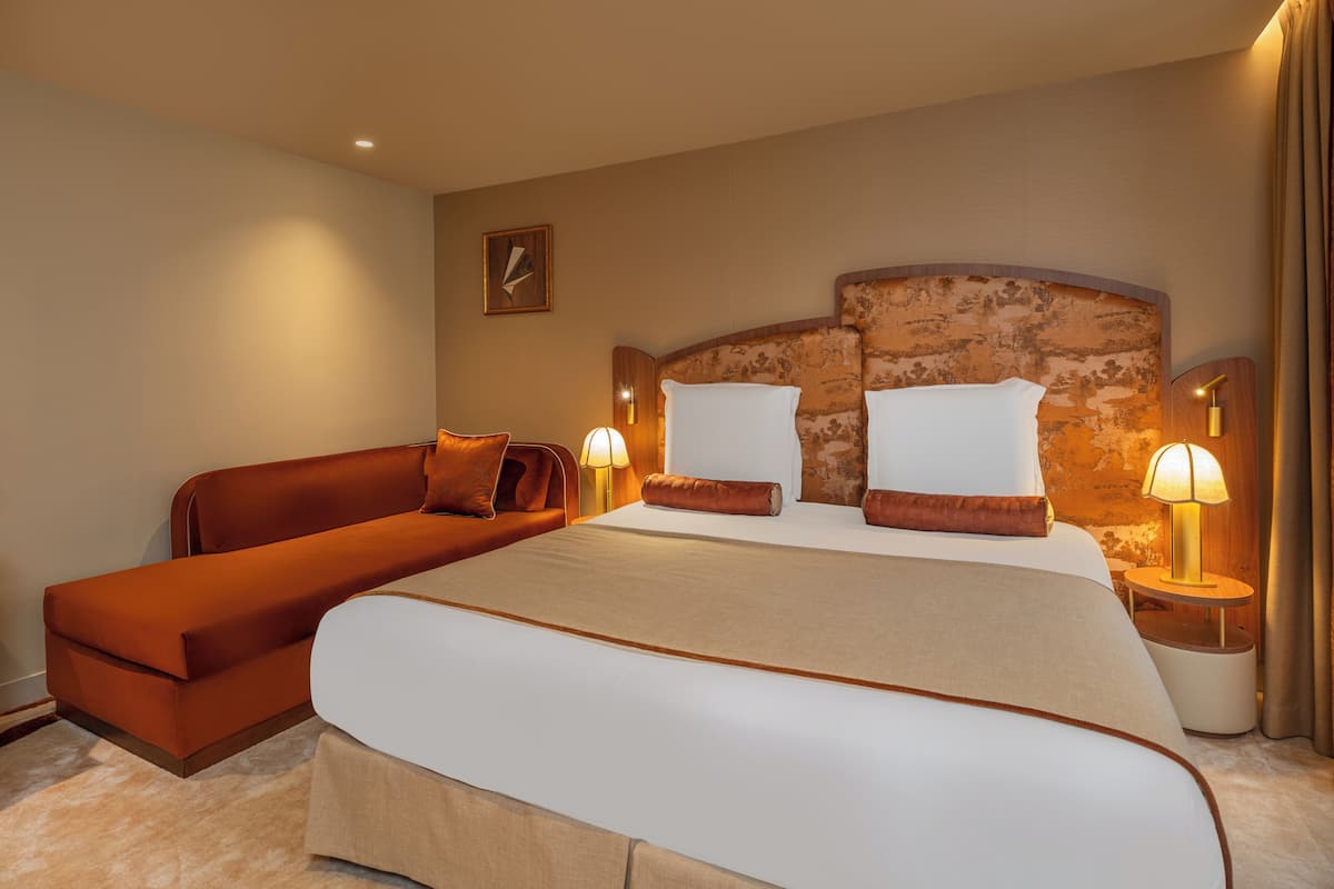Hotellihuone, jossa on suuri sänky, sohva, kaksi yöpöytävalaisinta ja seinäkello.