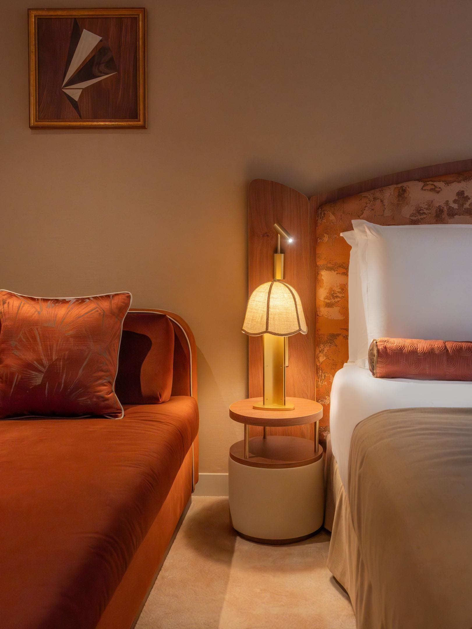 A hotel room with a bed, a nightstand, a lamp, and a painting on the wall.