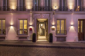 A historic building with a grand entrance, a staircase leading to an upper floor, and a red fire alarm on the wall. - Hotel Magda Champs Elysées (Paris)