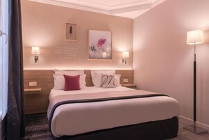 A hotel room with a large bed, two bedside lamps, a framed picture on the wall, and a floor lamp.