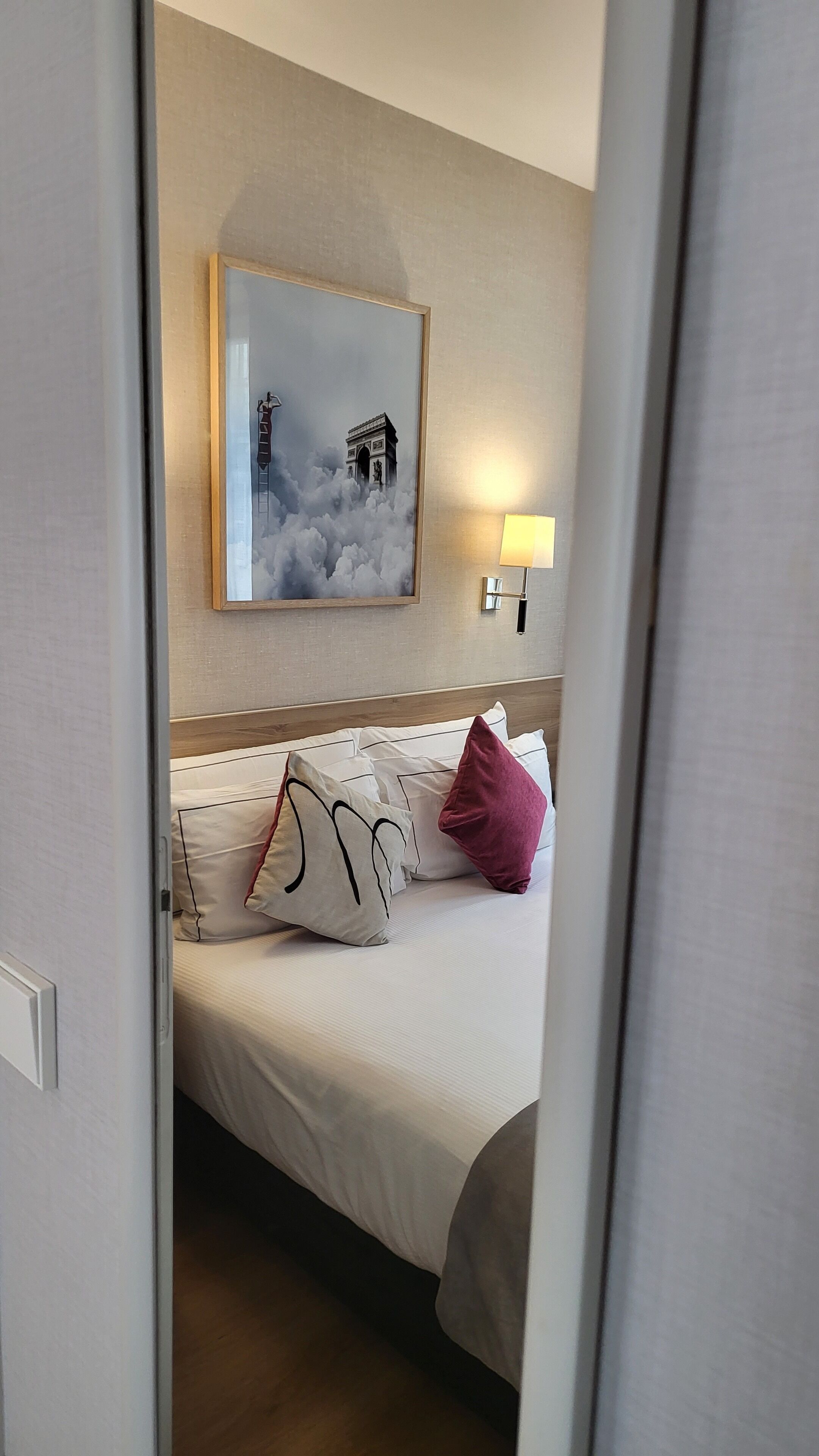 A hotel room with a bed, pillows, a framed picture on the wall, and a bedside lamp.