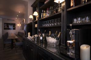 Eine Bar mit einer langen Theke, Regalen voller Flaschen und Gläsern und einer Kerze rechts.