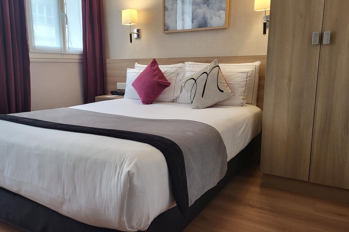 A hotel room with a large bed, a nightstand, a lamp, and a painting on the wall.