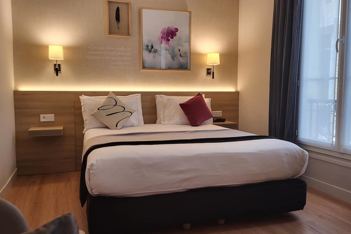 A neatly arranged hotel room with a large bed, two bedside lamps, a framed quote on the wall, and a window with a view.