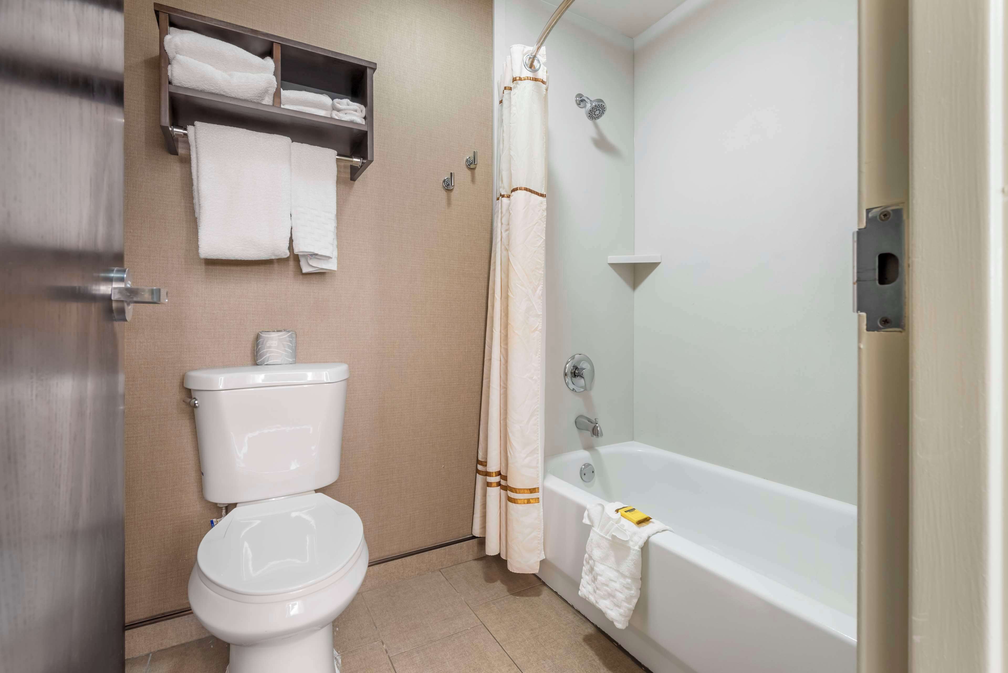 Un baño con inodoro, repisas con toallas y una bañera.