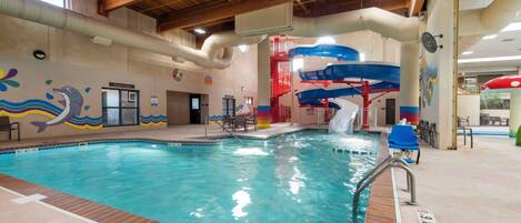 An indoor swimming pool with a water slide, wooden ceiling beams, and a colorful mural on the wall.