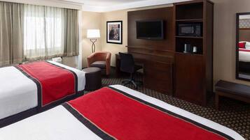 A hotel room with two beds, a desk, a chair, a television, and a microwave.