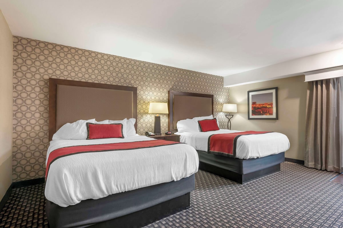 Ein Hotelzimmer mit zwei Betten, jeweils mit Kopfteil, einem Nachttisch mit Lampe, einem gerahmten Bild an der Wand und einem gemusterten Teppich.