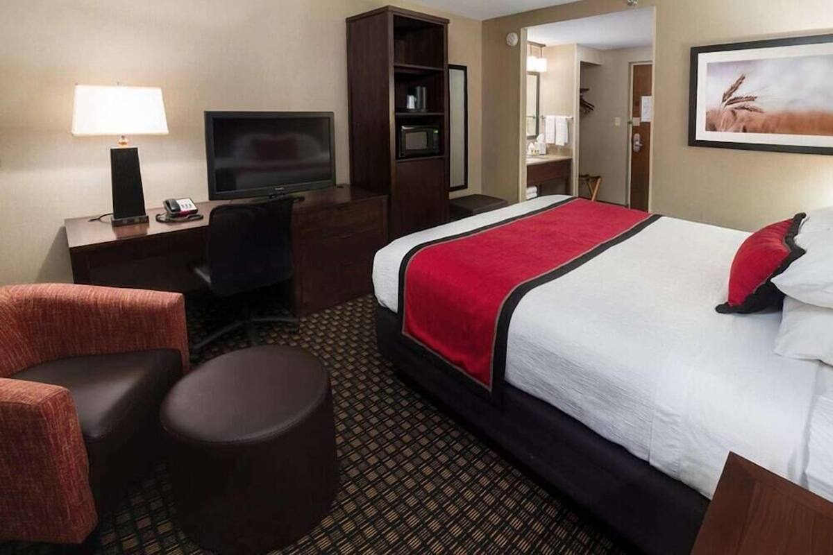 A hotel room with a large bed, a desk with a TV, a chair, a small round table, and a wardrobe.