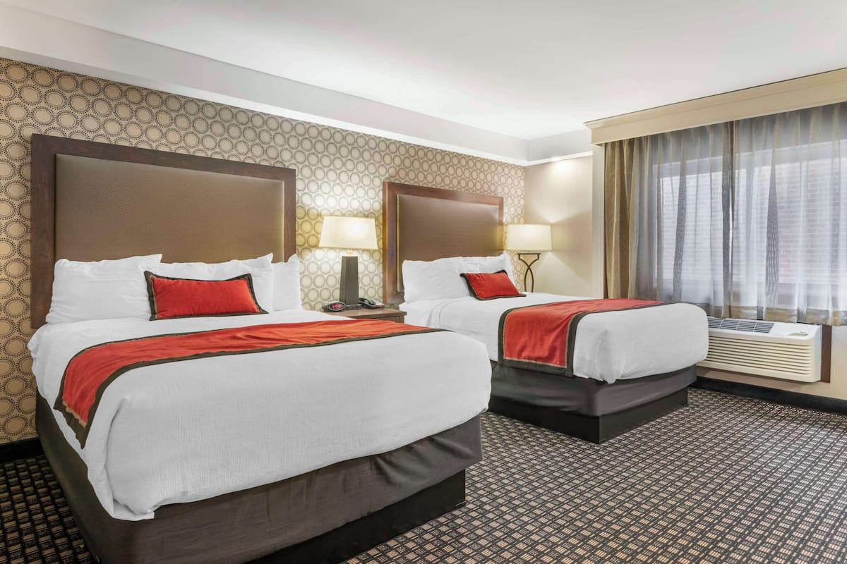 Ein Hotelzimmer mit zwei Betten, strukturiertem Wandpapier und einem großen Fenster mit Vorhängen.