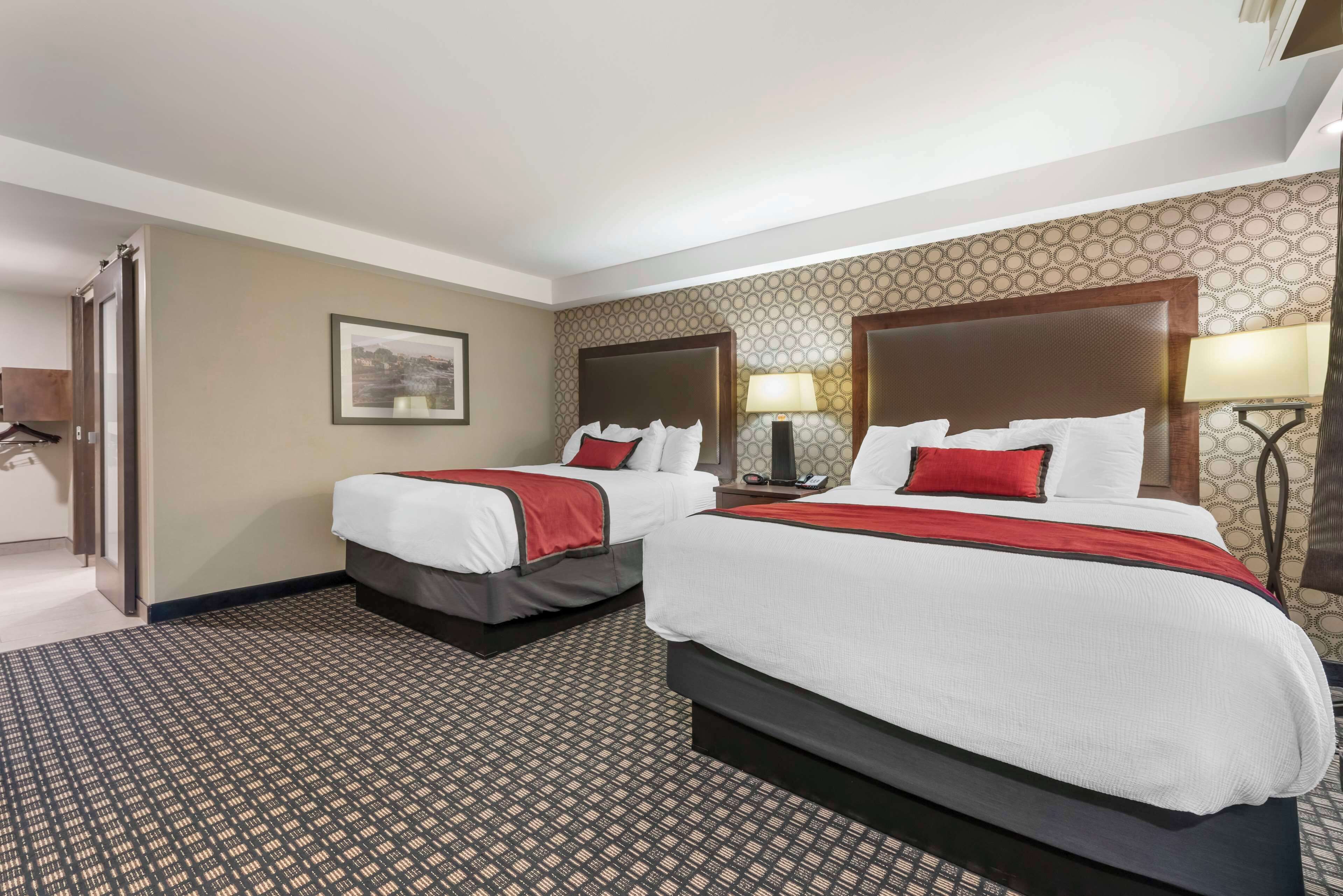 A hotel room with two beds, each with a headboard, a bedside table, and a lamp.