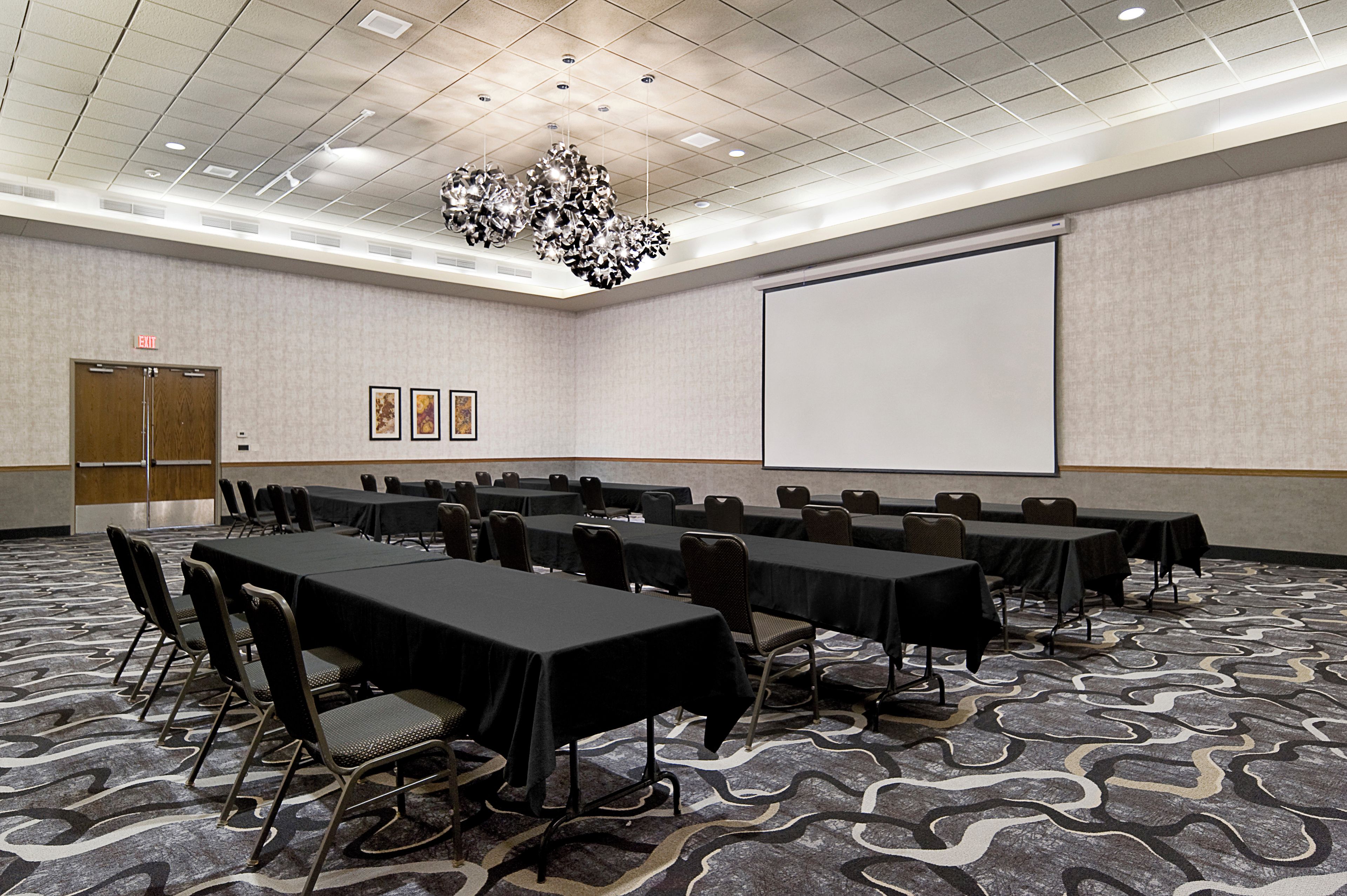 A conference room with tables and chairs, a projector screen, and an exit sign.