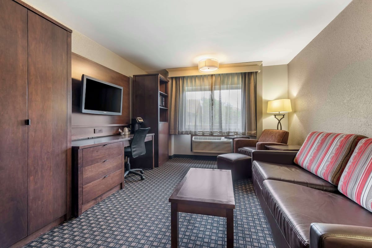 Ein Hotelzimmer mit großem Kleiderschrank, Schreibtisch mit Stuhl, einer Couch, einem Fernseher und einem Fenster mit Vorhängen.