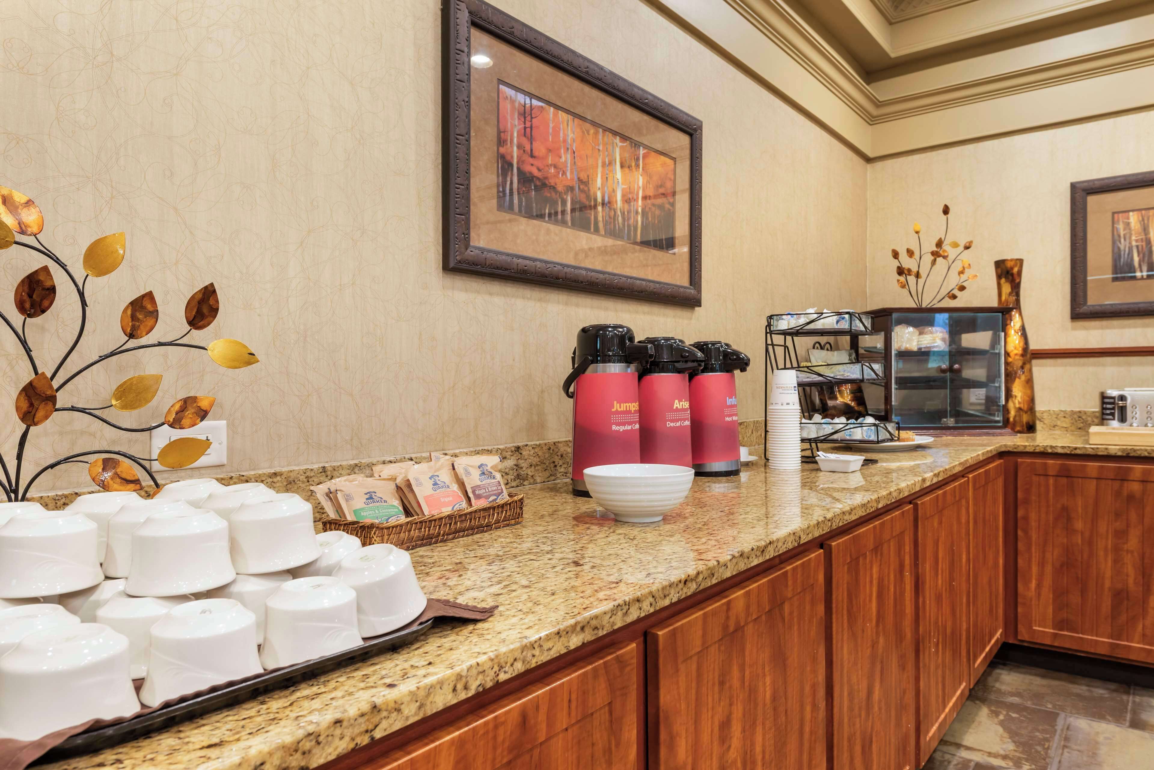Een hotelkeuken met een marmeren aanrecht, koffiezetapparaten en een ingelijst schilderij aan de muur.