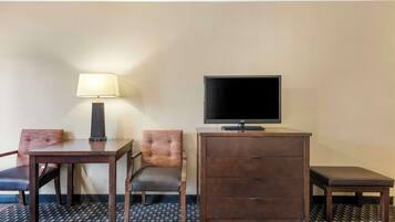 A hotel room with a bed, a desk, a chair, a TV, a lamp, and a dresser.