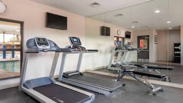 Un gimnasio con cintas de correr, una banca de pesas y una televisión montada en la pared.